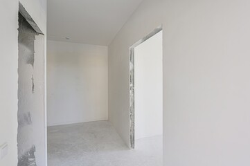 empty, all-white room with a doorway leading to another space. The walls are plain, and the floor is bare. Minimalist and clean aesthetic.