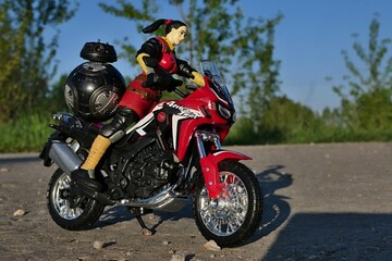 Naklejka premium GI JOE action figure of female intelligence agent Jinx riding on Honda Africa Twin motorbike, Star Wars imperial astromech BB-9e on rear seat. Spring afternoon sunshine. 