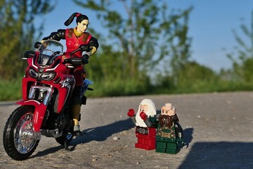 Obraz premium GI JOE action figure of female intelligentce agent Jinx, version 2004, standing with japanese dual sport motorbike Honda Africa Twin on asphalt road, greeting two LEGO dwarfes Balin and Dwalin on road