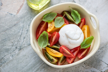Burrata cheese with heirloom tomatoes and green basil, horizontal shot on a grey granite background, high angle view