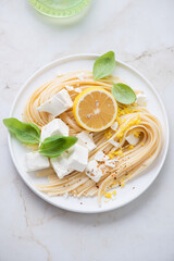 Plate of lemon linguine with feta cheese and basil on a light-beige marble background, top view, vertical shot