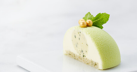 Banner Image of Cut Green Velvet Mousse Cake with Mint and Golden Pearls on White Plate.