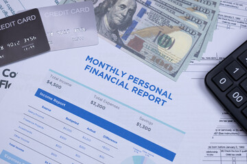 Monthly personal financial report with credit cards, US dollars, and a calculator on a desk, representing budgeting and money management.