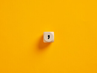 Wooden cube showing comma sign on yellow background