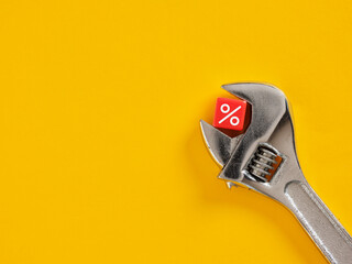 Adjustable wrench is holding red percentage sign on yellow background