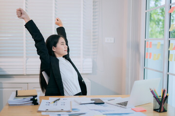 Asian female accountant stretches to relax after being tired from sitting in a chair while working...