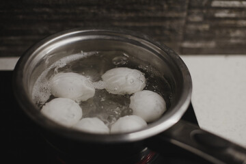 White eggs boiling in a small pot on a ceramic stove top