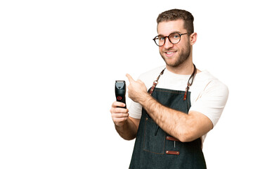 Barber man in an apron over isolated chroma key background pointing back