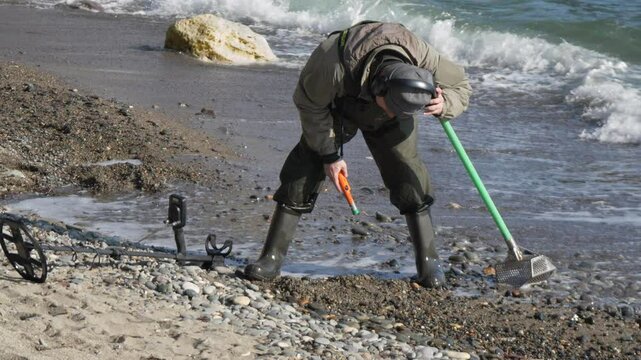 MetalDetecting Beach Treasurehunting: Person uses metal detector, shovel on pebble beach during daytime