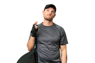 Young sport man with sport bag over isolated chroma key background with fingers crossing and wishing the best