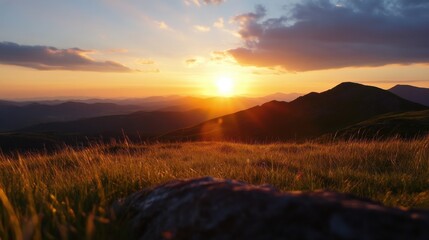 Obraz premium Golden sunset over a vast mountain range, casting long shadows across the grassy landscape. A foreground rock adds texture to the serene scene. : Generative AI
