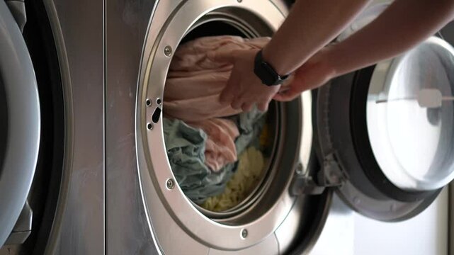 A person removes freshly washed laundry from a front-loading washing machine in a bright laundry room, emphasizing cleanliness, domestic routine, and household efficiency.