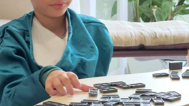 The Southeast Asian boy is playing a domino game with his mother in the living room.
