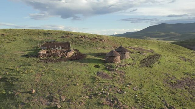 Aerial orbit around rural Basotho homestead, thatched stone rondavels with enclosures for livestock