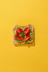 Avocado toast with boiled eggs, cherry tomato and cucumber on a yellow background
