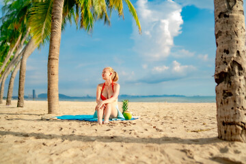 Joyful female enjoying the sunshine while seated on a pristine beach in a red bikini. Her smile radiates happiness, freedom, and a sunny coastal mood.