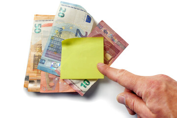 Hand pointing to European banknotes on a white surface and yellow paper note on top. Monthly bill payments reminder for house rent, electricity, water and phone. Rising cost of living in Euro Union