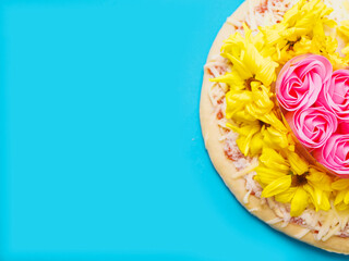 Pink roses in heart love shape and white chamomile flowers on top of a pizza and on blue background. Abstract conceptual art. Selective focus.