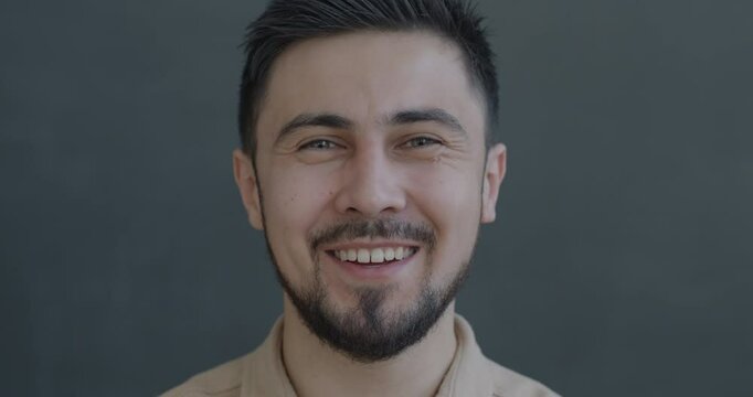 Slow motion portrait of joyful young biracial man laughing looking at camera on gray color background. People and positive emotion concept.
