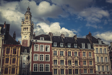Fototapeta premium Colorful historic facades line the town square in Lille, France. Elegant belfry clock tower and dramatic sky in background.