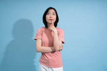 Thoughtful Asian woman with a pink shirt thinking against a light blue background during a creative...