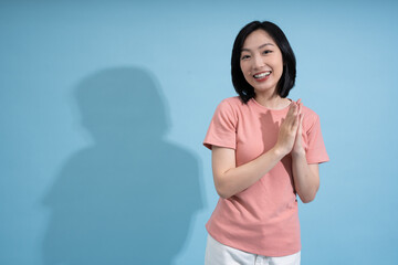 Smiling young Asian woman in a pink t-shirt poses against a blue background while engaging in a...