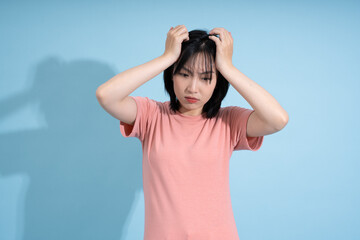 Young Asian woman expressing frustration in casual setting against light blue backdrop while...
