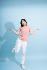 Young Asian woman standing playfully with arms outstretched against a blue background in a casual outfit during daylight