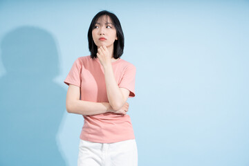 Thoughtful young woman in casual attire poses against light blue backdrop while contemplating ideas...