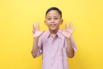 Smart asian schoolboy standing while showing nine fingers. Isolated on yellow with copyspace