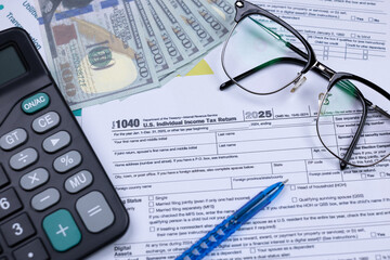 Tax documents, calculator, pen, cash, and glasses arranged on a desk, representing financial planning and tax preparation.