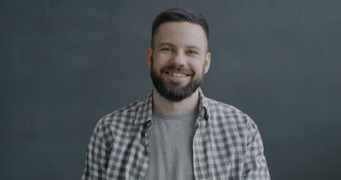 Slow motion portrait of friendly young man waving hand smiling looking at camera on black color background. People and expression concept.