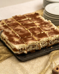 A classic Italian tiramisu dessert cut into square portions, topped with cocoa powder, presented on a festive golden tablecloth.