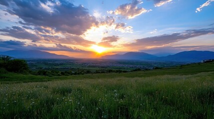 Obraz premium Serene sunset over a vast valley, with vibrant orange and purple hues painting the sky above rolling green hills and a distant town. : Generative AI