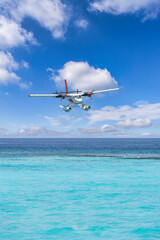 Fototapeta premium Amazing travel background Maldives seaplane landing near luxury resort perfect tropical getaway. Exotic transportation seaplane over calm ocean lagoon, azure turquoise sea water sunny blue sky clouds