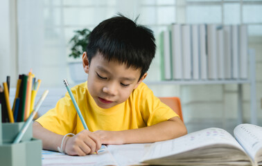 Cute 6-8 year old school boy doing homework at home on weekends. Writing homework diligently with a pencil. Very happy doing homework. Home learning. Online learning.