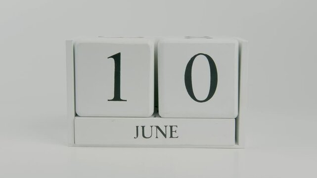 A hand turns a wooden calendar block from June 10th to June 11th on a white background, representing the quiet shift of days in early summer