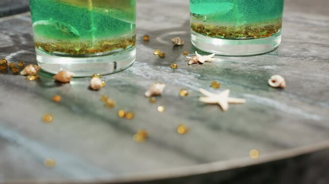 Decorating materials including small beads, star-shaped and shell-like items are scattered on kitchen work table beside tealight cups filled with green and golden wax mixture