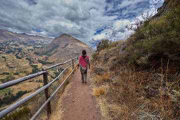 Fototapeta premium young woman admiring the ancient Inca Ruins of Pisac with Dramatic Mountain Landscape, Sacred Valley, Peru