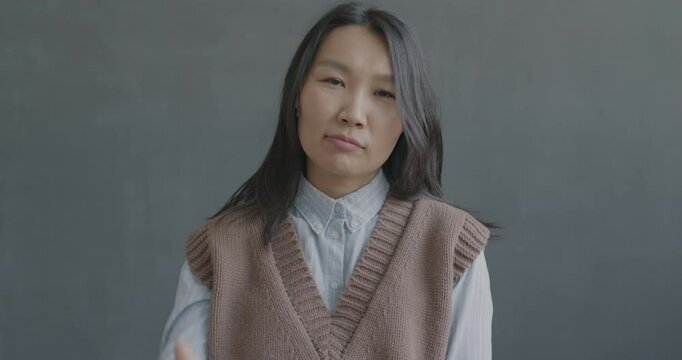 Slow motion portrait of unhappy Asian woman showing thumbs-down hand gesture and shaking head looking at camera on black color background.
