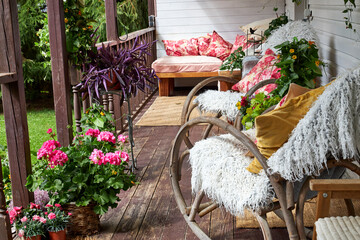 Fototapeta premium View of a modern-style summer veranda interior decorated with bright summer flowers, rattan rocking chairs, and a large pink sofa