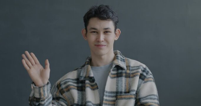 Slow motion portrait of cheerful Asian man waving hand smiling on gray color background. People and expression concept.