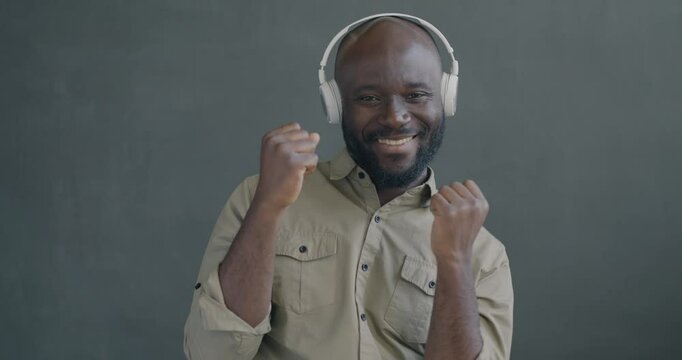 Slow motion portrait of happy African American man listening to music with headphones dancing looking at camera. People and entertainment concept.