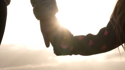 Mother and young daughter enjoy walking outdoor. Holding hands clasped together as they share...