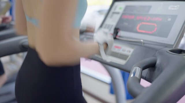 A woman running on a treadmill. The screen shows the time and distance. A man is also running on the same machine