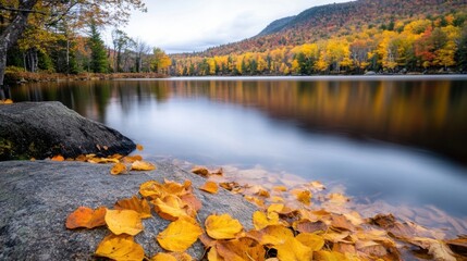 Obraz premium Autumn leaves gently drift onto a smooth rock beside a tranquil lake, reflecting the vibrant fall foliage of the surrounding hills. : Generative AI