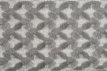 A detailed close-up reveals a textured, silver-toned surface with a repeating, abstract leaf-like...
