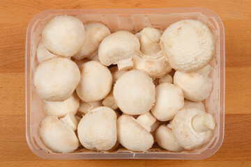 A top-down view of a clear plastic container filled with fresh white button mushrooms, ready for cooking