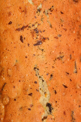 The textured surface of a freshly baked loaf cake with walnuts, raisins, chocolate pieces, and orange zest