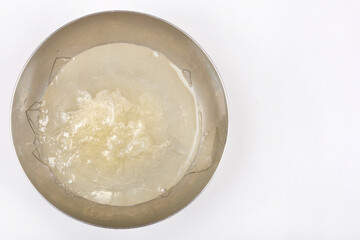 A top-down shot shows dissolved leaf gelatin in a round metal bowl filled with water, ready for incorporation into a recipe, against a light gray surface